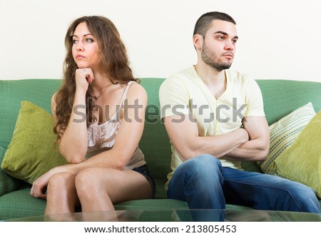 Young married couple sitting sad on sofa after quarrel at home