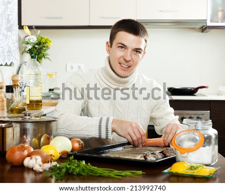 Happy guy putting  saltwater fish into sheet pan at kitchen table