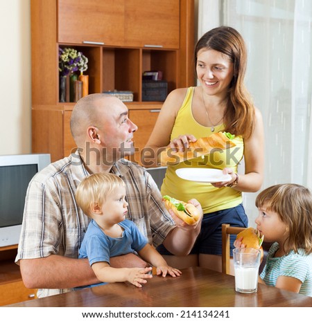 happy parents and two children having lunch with sandwiches at home together