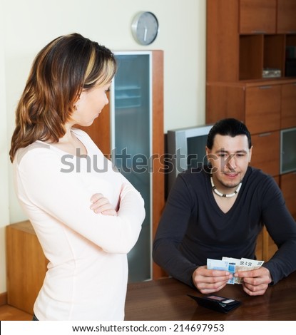 Financial problems in family. Man counting cash, woman watching him in home