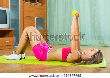 Active young woman working out with dumbbells at home