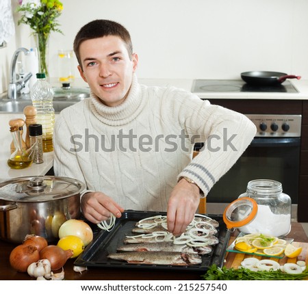 Happy guy cooking trout fish with onion in baking sheet at home kitchen