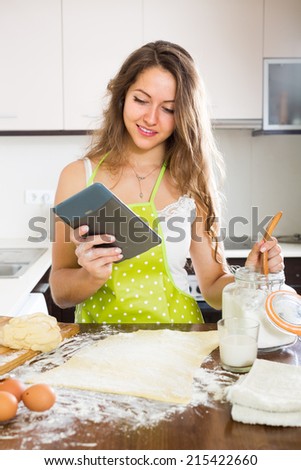 Young housewife in apron cooking with tablet at home kitchen