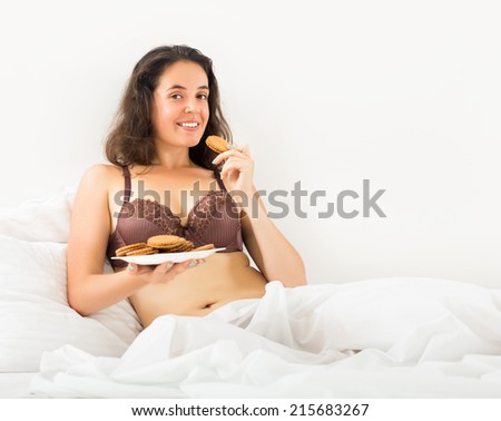 Long-haired woman eating  chocolate chip cookies in bed
