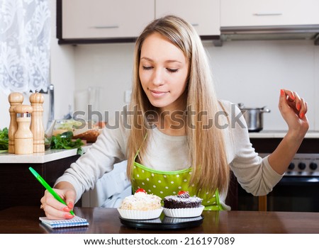 Smiling woman weighing cakes on kitchen scales at kitchen