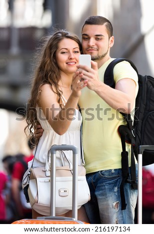 Happy man and woman with luggage doing selfie during city tour at vacation