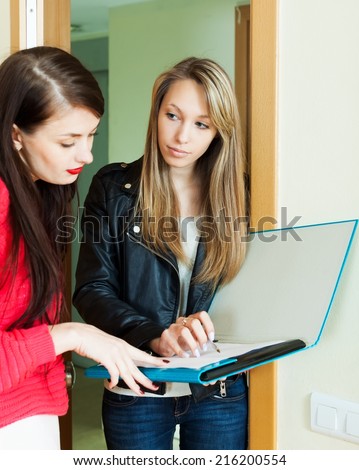 Young woman answer questions of smiling girl with papers at door at home