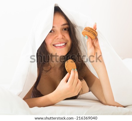 Young woman eating chocolate chip cookies in her bed and smiling