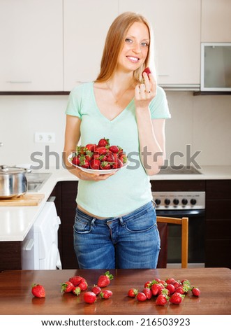 Happy blonde long-haired woman eating strawberries