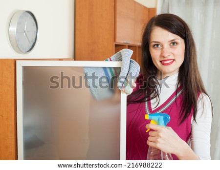 Smiling brunette girl cleaning  glass door of furniture