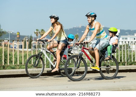 Sporting young father, mother and two children in baby bicycle seats summer day