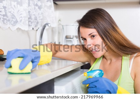 Happy young woman washing  furniture in kitchen at home