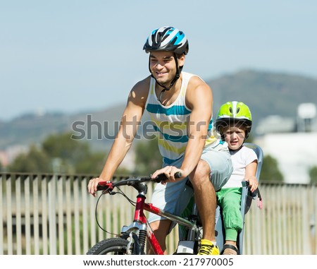 Smiling young father with daughter in helmets cycling though street