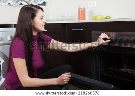Smiling woman cooking pie in the oven in home kitchen