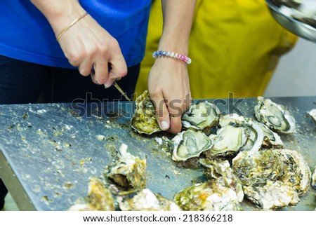 worker opening oysters at oyster farm or restaurant