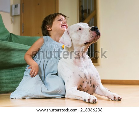 Happy smiling little girl with big white dog lying on the floor at home
