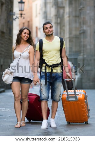 Man and woman in shorts with luggage walking through city street