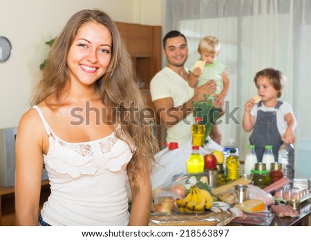 Cheerful mother, father and daughters of four with bags of food at home. Focus on woman