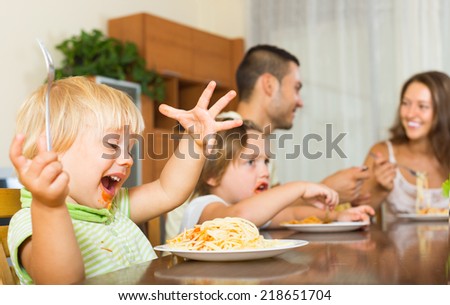 Smiling young family of four having lunch with spaghetti at home. Focus on girl