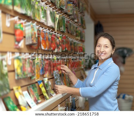 Smiling mature woman chooses packaged seeds at store