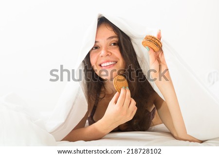 Smiling young woman eating chocolate chip cookies in her bed and smiling