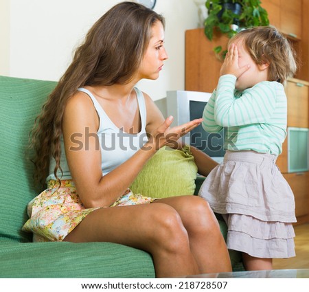 Young serious mother scolding crying child at home interior