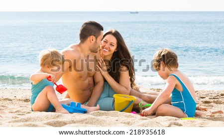 Young mother and father with two kids playing on the beach with sand