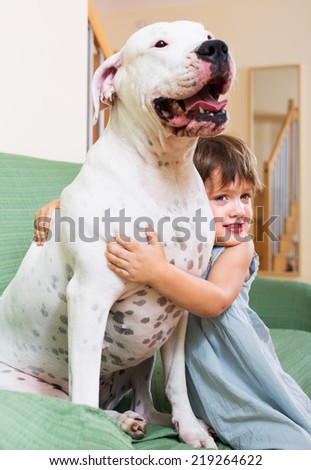 Happy smiling little girl hugging big white dog at home. Focus on girl