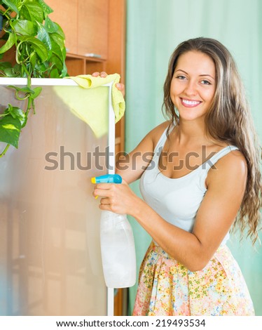 Happy smiling girl cleaning glass door of furniture at home