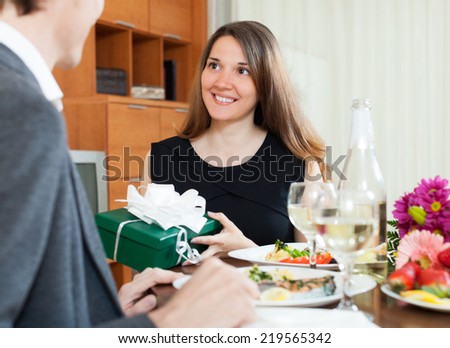 Pretty woman giving present box to man at table during romantic dinner