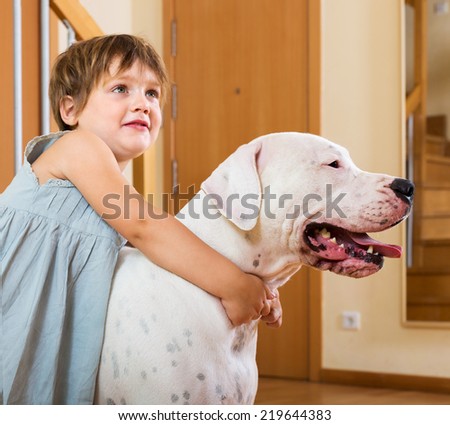 Happy smiling cute little girl hugging big white dog at home