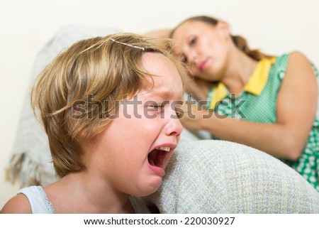 Crying little girl and upset mother sitting on couch at home