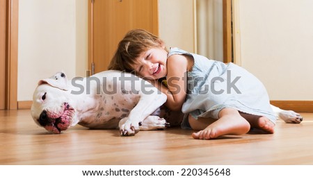 Smiling playful cute little girl hugging big white dog at home
