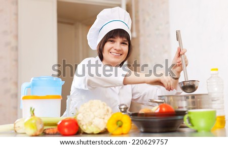 Female cook with ladle adds salt into soup pan at kitchen