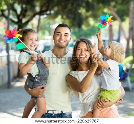 Young parents with children playing windmills in park on vacation day