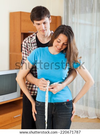 Guy measuring waist of girlfriend with measuring tape at home