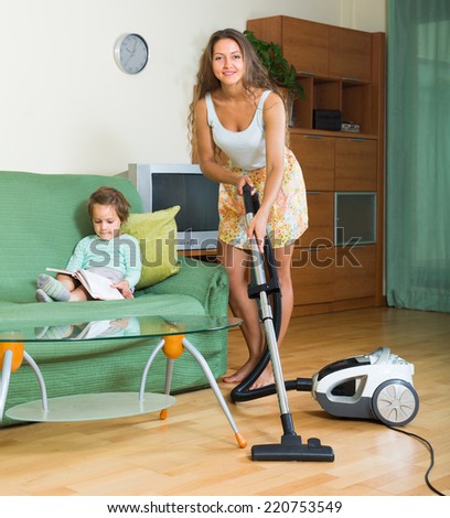 Young mother and little daughter cleaning living room with vacuum cleaner