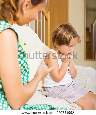Mother scolding crying little girl at sofa