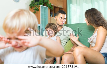 Young husband and wife sitting on the couch and quarreling in the presence of children