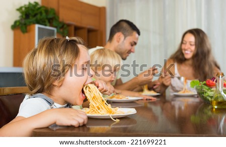 Young family of four eating with spaghetti at table. Focus on girl
