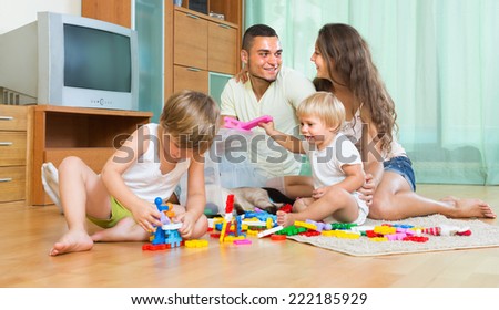 Happy young parents and two little daughters playing with plastic toys in home. Focus on man