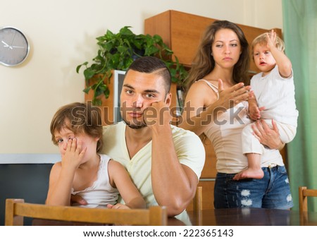 Young family with two children on hands having quarrel in home interior