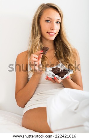 Girl eating sweet chocolate on white sheet in her bedroom