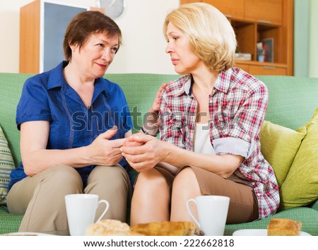 Two elderly female sitting at the table with tea and sharing bad news