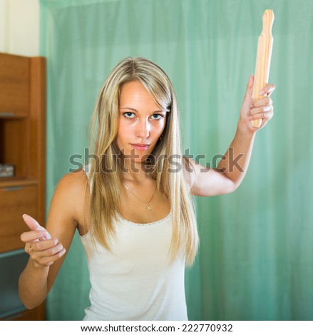 Furious girl swinging her arm with rolling-pin in home interior