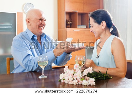 Mature man presenting woman jewel in box  at table
