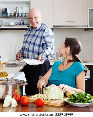 Loving elderly man and mature woman  doing housework together in home kitchen