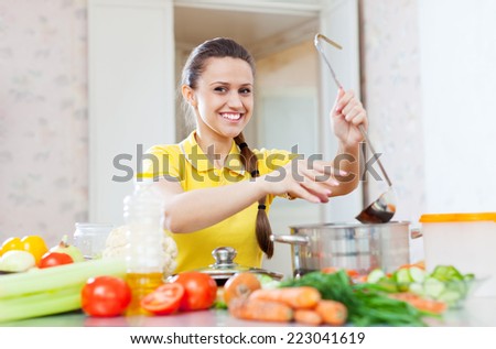 Happy young woman adds spice or salt in saucepan at domestic kitchen