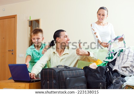 Happy family of three choosing resort on  internet and packing suitcases at home