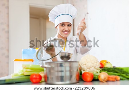 female cook in toque works with ladle at commercial kitchen